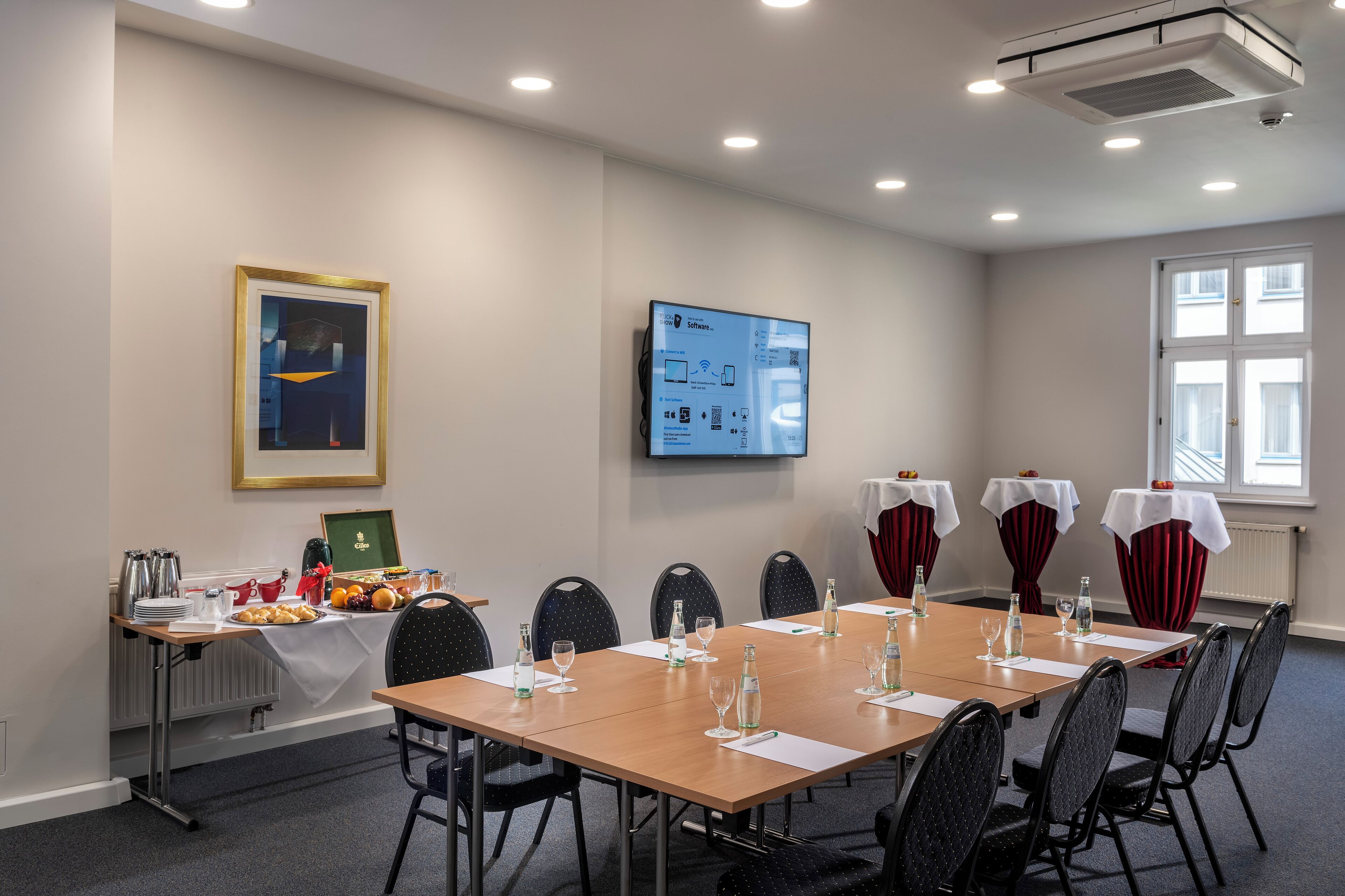 A conference room with a long table, chairs, a projector screen, and a window.
