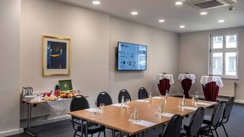 A conference room with a long table, chairs, a projector screen, and a window.