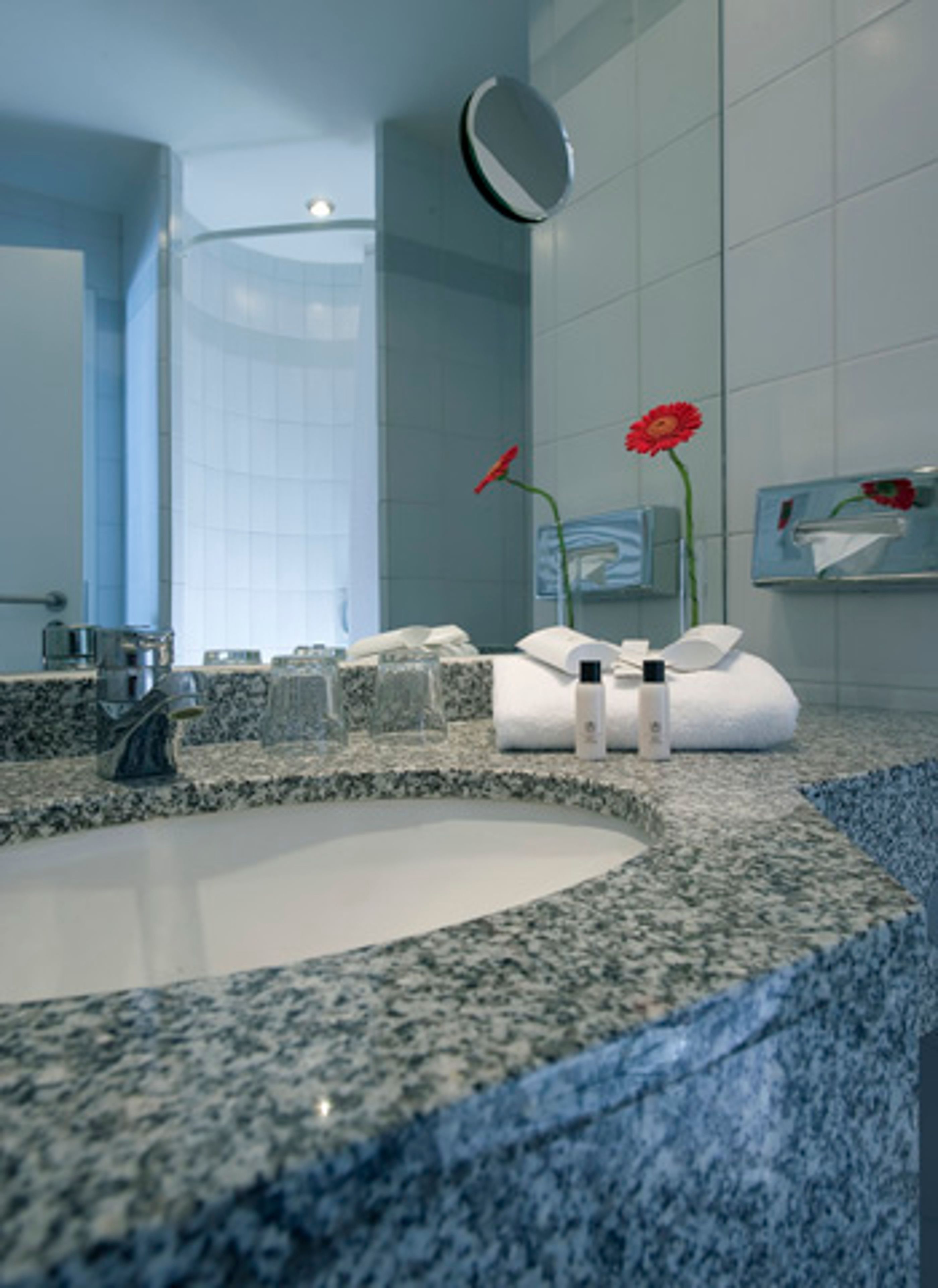 A modern bathroom with a granite countertop sink, a round mirror, and a towel rack.
