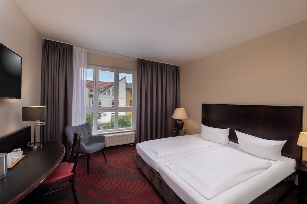 A hotel room with a large bed, a desk with a chair, a TV, and a window with curtains.
