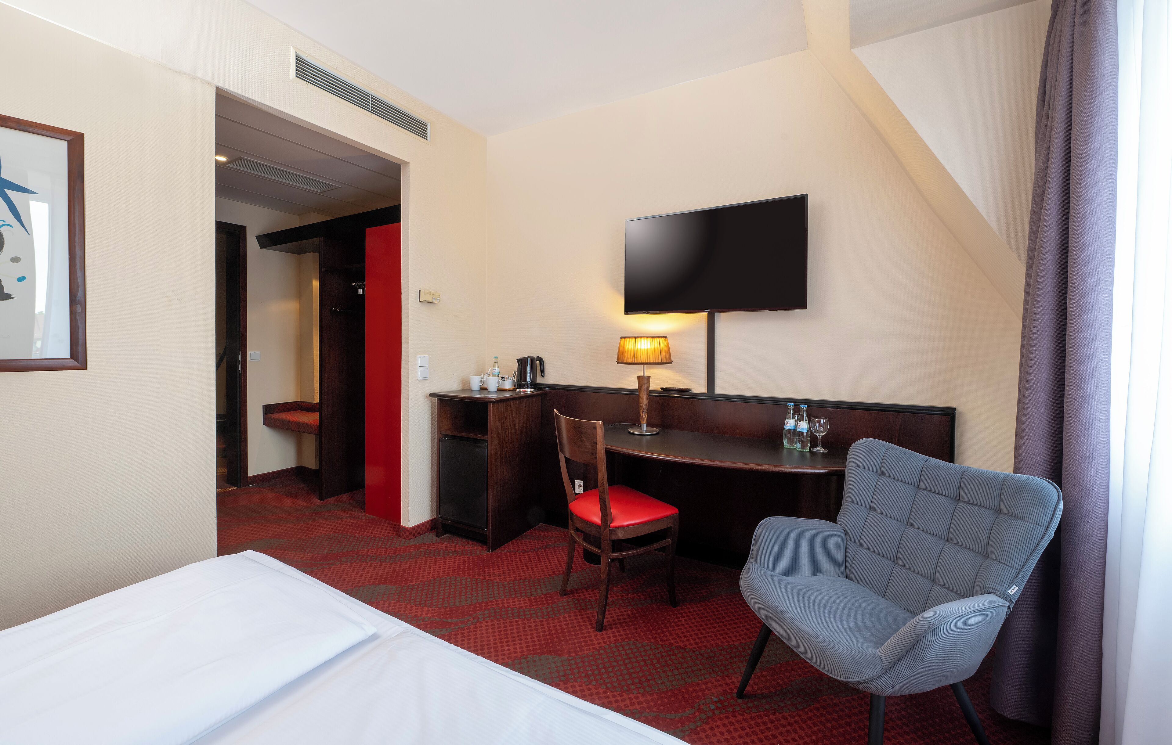 Ein Hotelzimmer mit einem Bett, einem Schreibtisch, einem Sessel, einem Fernseher und einem roten Teppichboden.