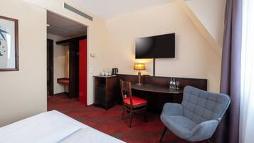 Ein Hotelzimmer mit einem Bett, einem Schreibtisch, einem Sessel, einem Fernseher und einem roten Teppichboden.
