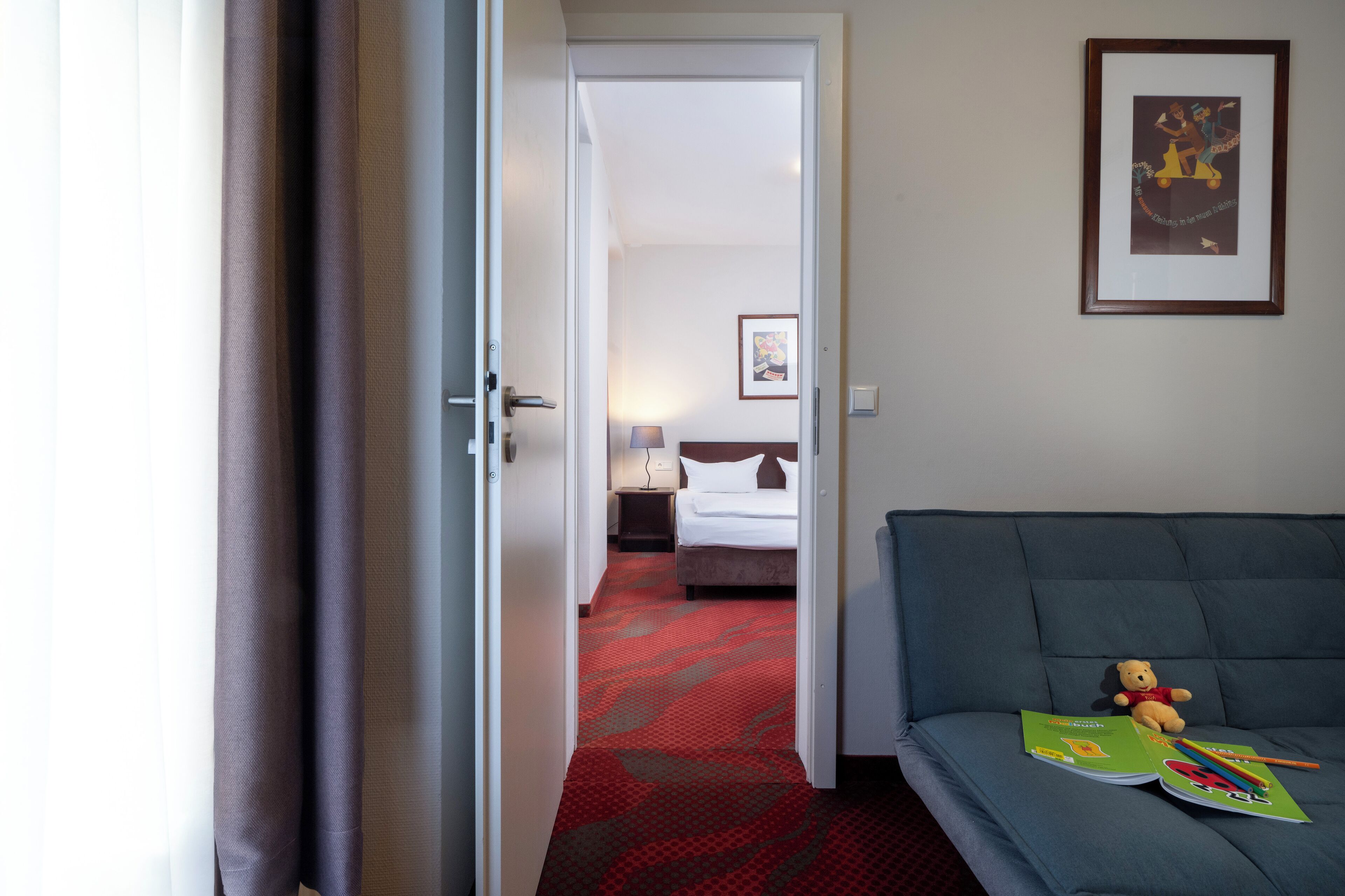 A hotel room with a bed, a sofa, and a teddy bear on the sofa.
