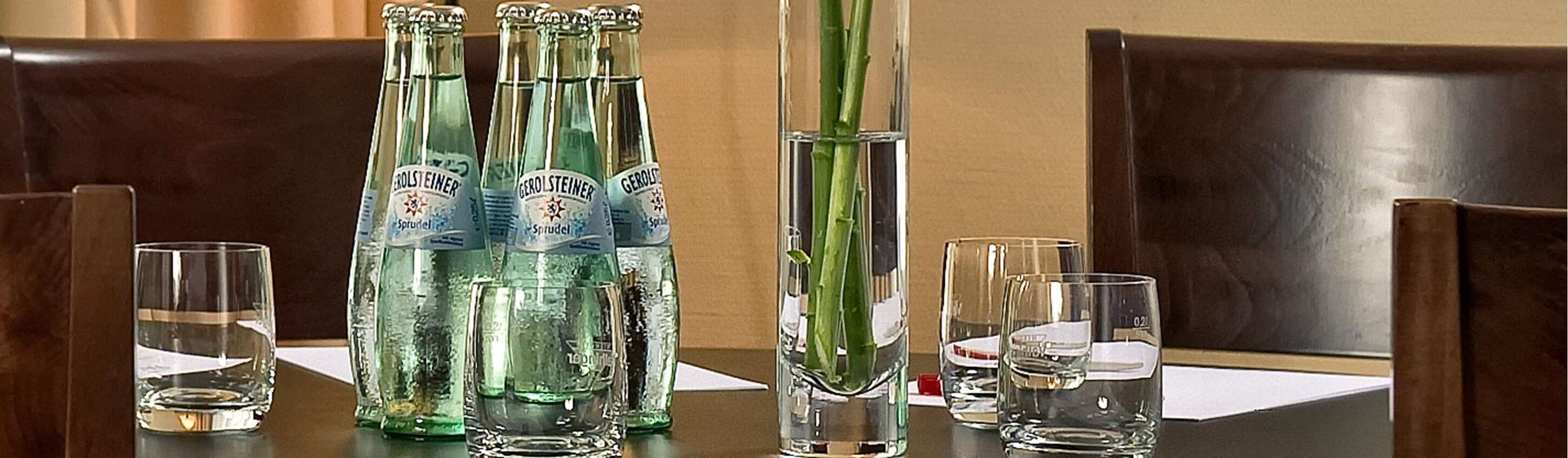 Un tavolo con diverse bottiglie di Gerolsteiner Sprudel e bicchieri, in una sala da pranzo con sedie di legno.