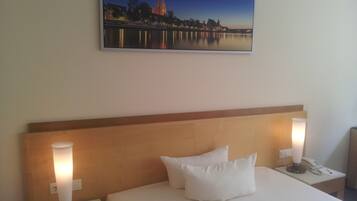A hotel room with a bed, two bedside lamps, a nightstand, a painting of a cityscape, and a telephone on the nightstand.