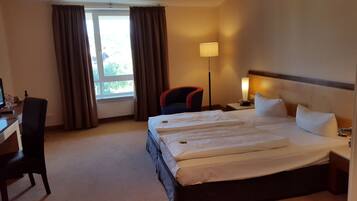 Habitación de hotel con una cama grande, un escritorio, una silla, una lámpara y una ventana con cortinas.