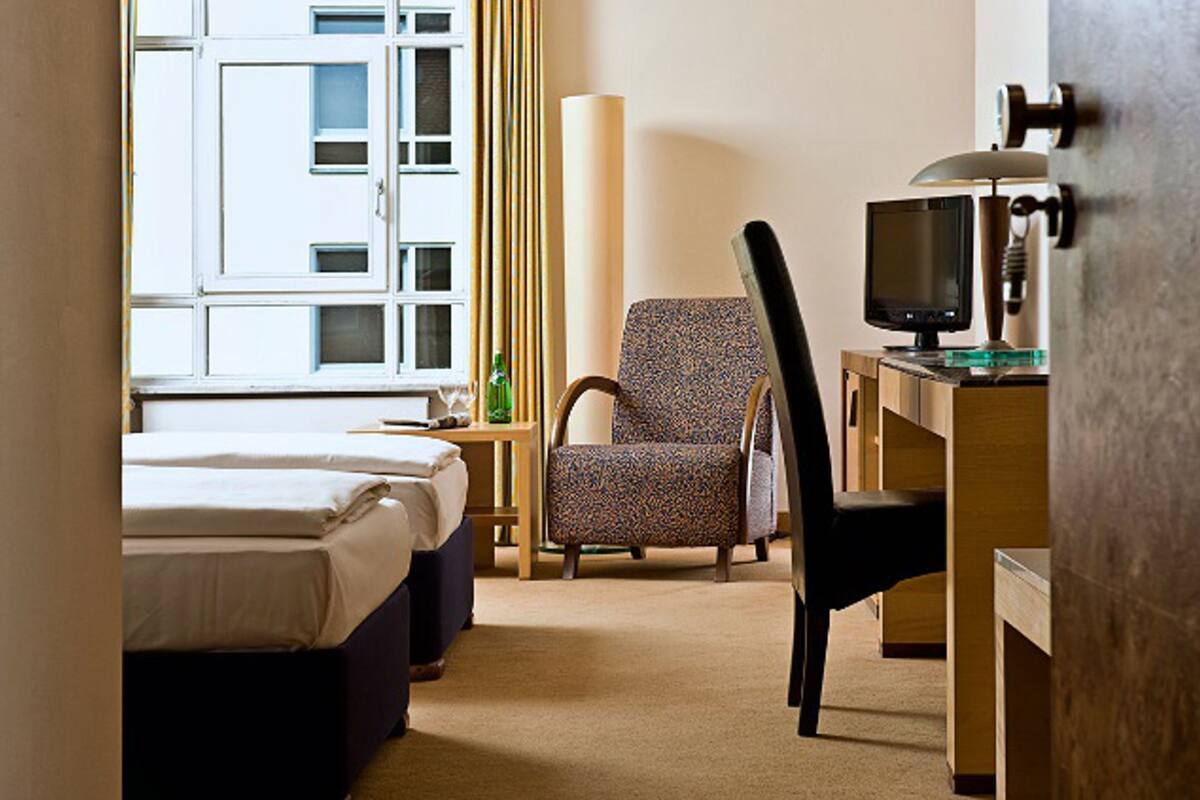 A hotel room with two beds, a chair, a desk with a computer, and a window with curtains.
