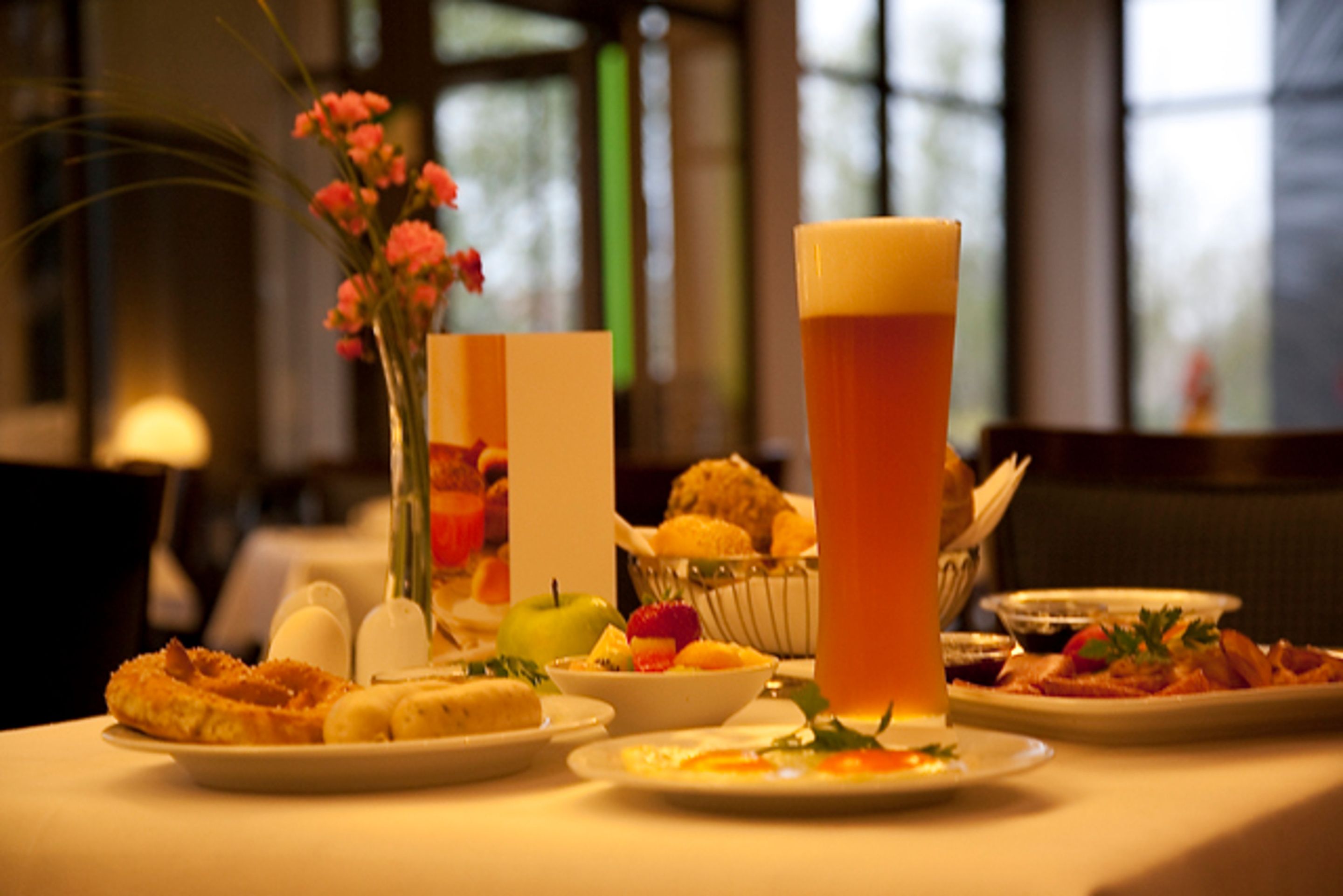 A dining table with various dishes, a tall glass of beer, and a vase with flowers.