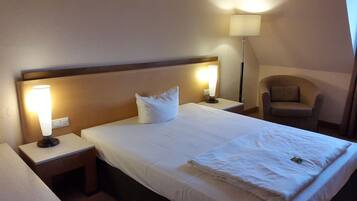 Ein Hotelzimmer mit einem ordentlich bezogenem Bett, zwei Nachttischlampen, einem Sessel und einer Stehlampe.