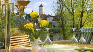 A wooden table set with wine glasses, a vase with yellow flowers, and a bench. - Sorat Insel-Hotel Regensburg (Regensburg)