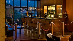 A bar area with a view of the cityscape through large windows, wooden bar counter, and seating arrangement. - Sorat Insel-Hotel Regensburg (Regensburg)