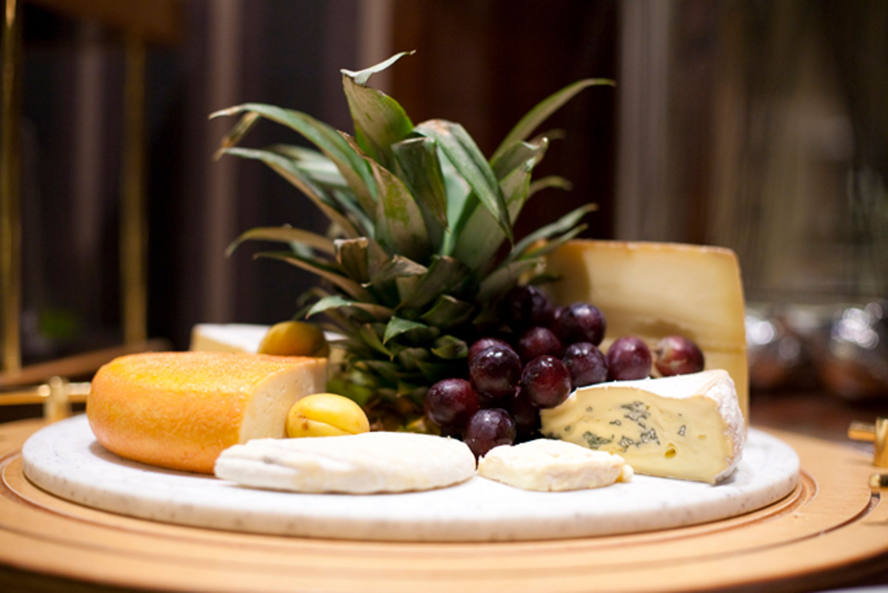 Una tabla de quesos con diferentes tipos de queso, uvas y una piña sobre una tabla de madera redonda.