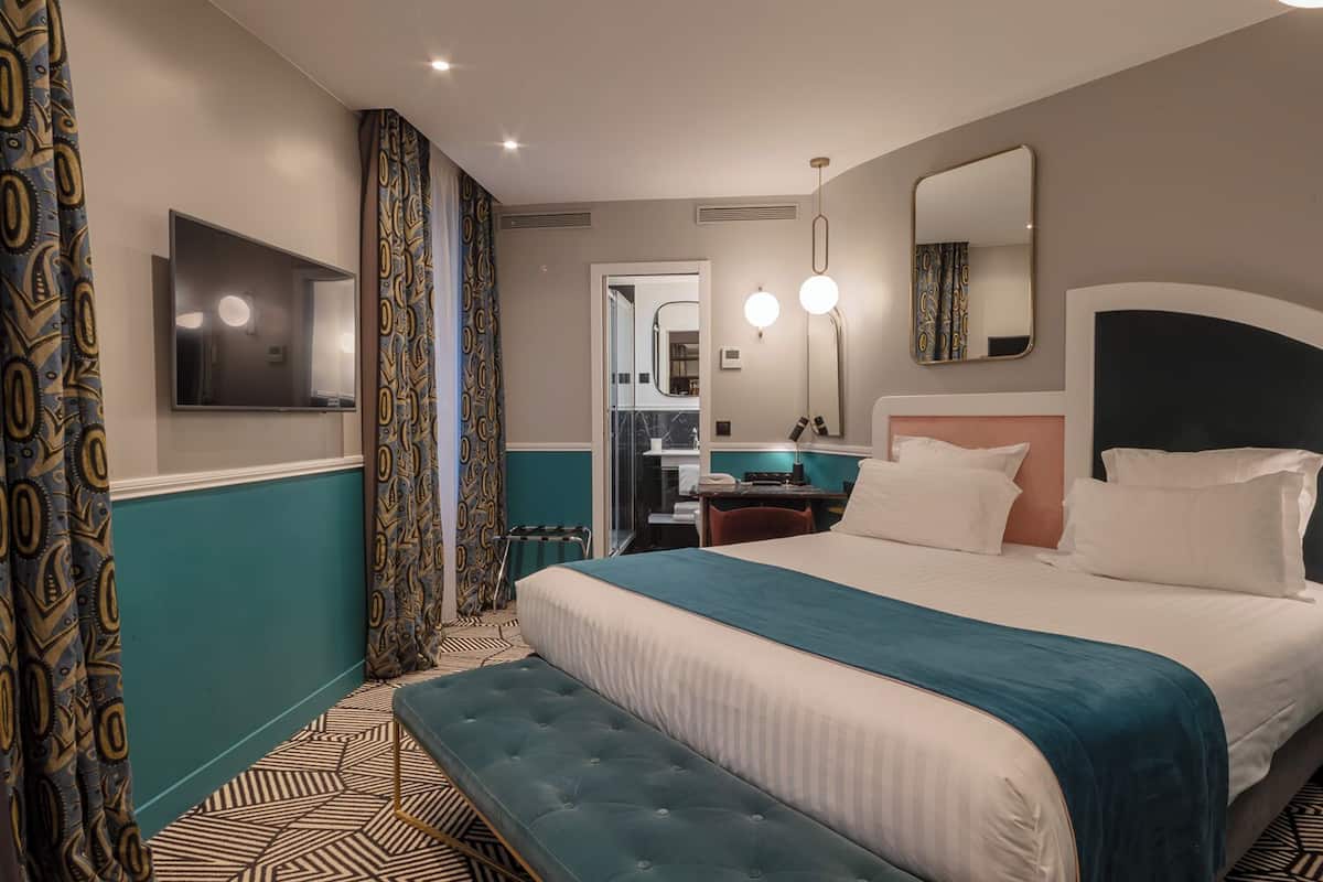A hotel room with a large bed, a bench, a desk, and a mirror.