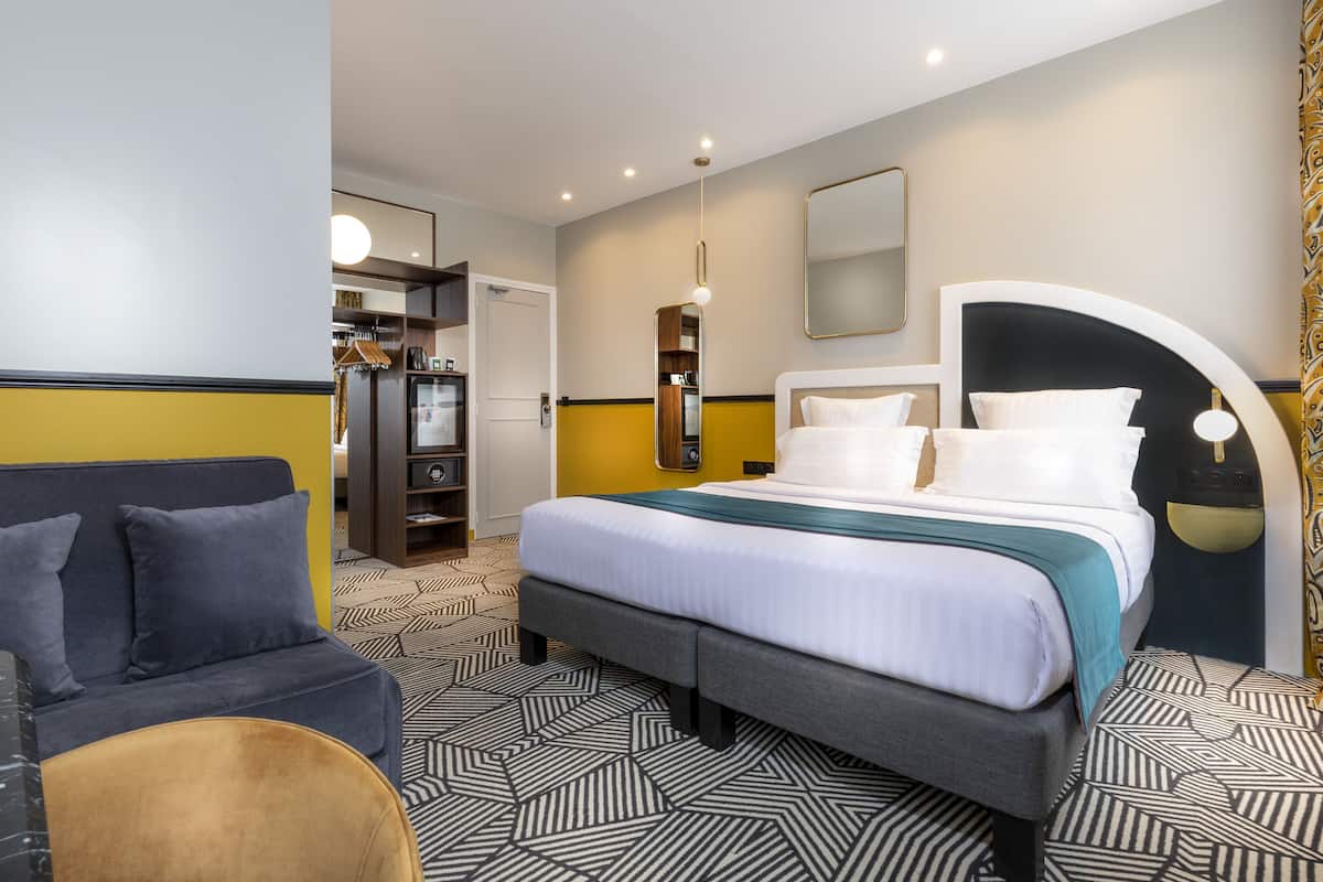 A modern hotel room with a bed, a sofa, a wardrobe, and a mirror.