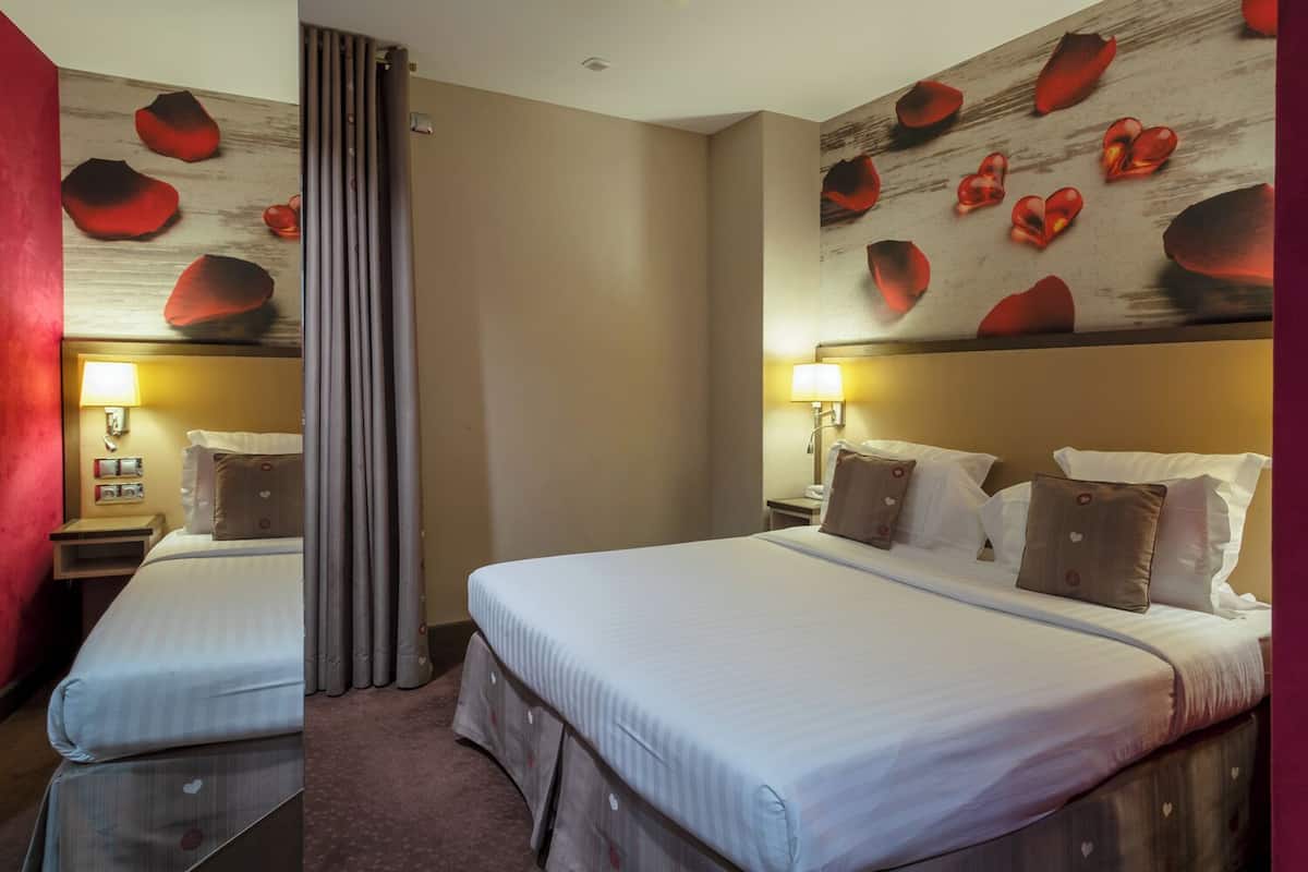 A hotel room with two beds, a wooden headboard with heart-shaped decorations, a red accent wall, and a mirror.