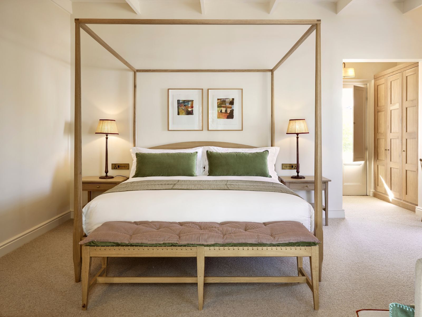 A four-poster bed with a bench in front, two bedside lamps, and two framed pictures on the wall.