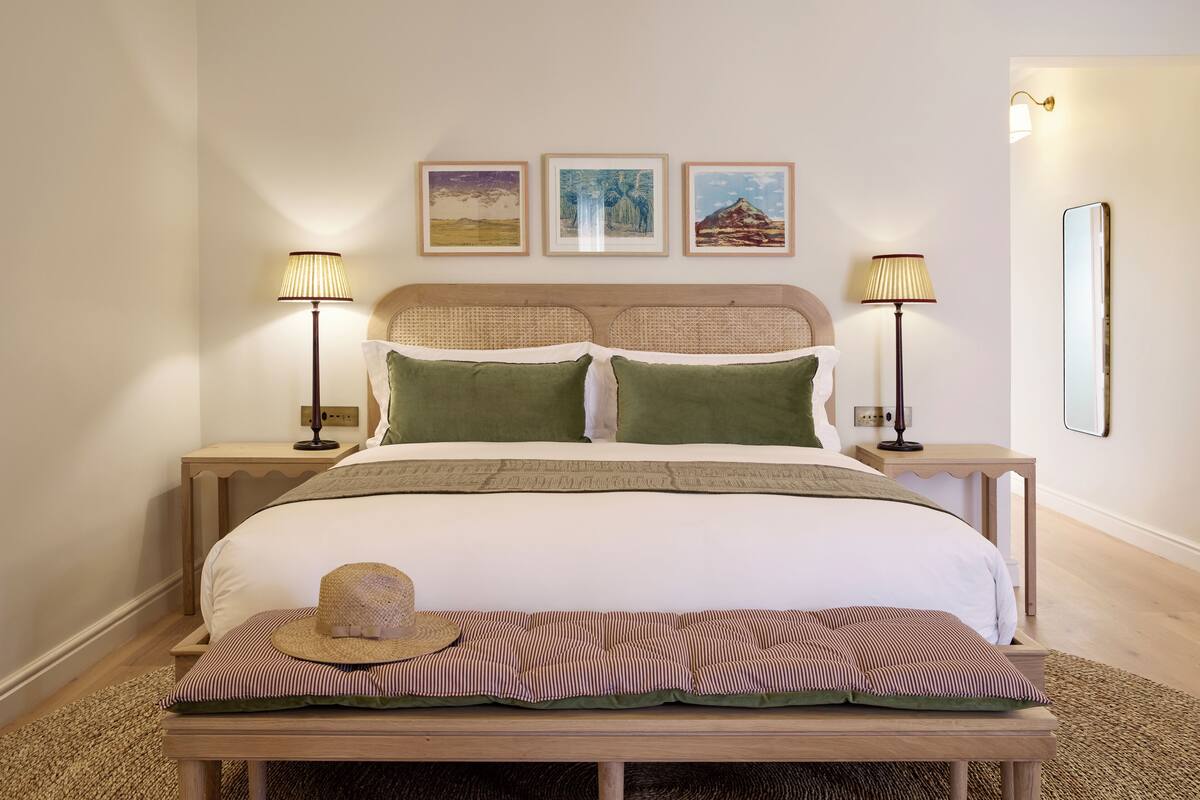 Ein ordentlich eingerichtetes Schlafzimmer mit einem Bett, zwei Nachttischen, einer Bank und drei Wandbildern.