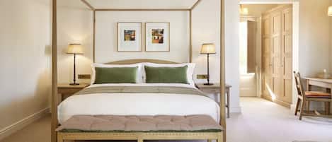 A four-poster bed with a bench in front, two bedside tables with lamps, and two framed pictures on the wall.
