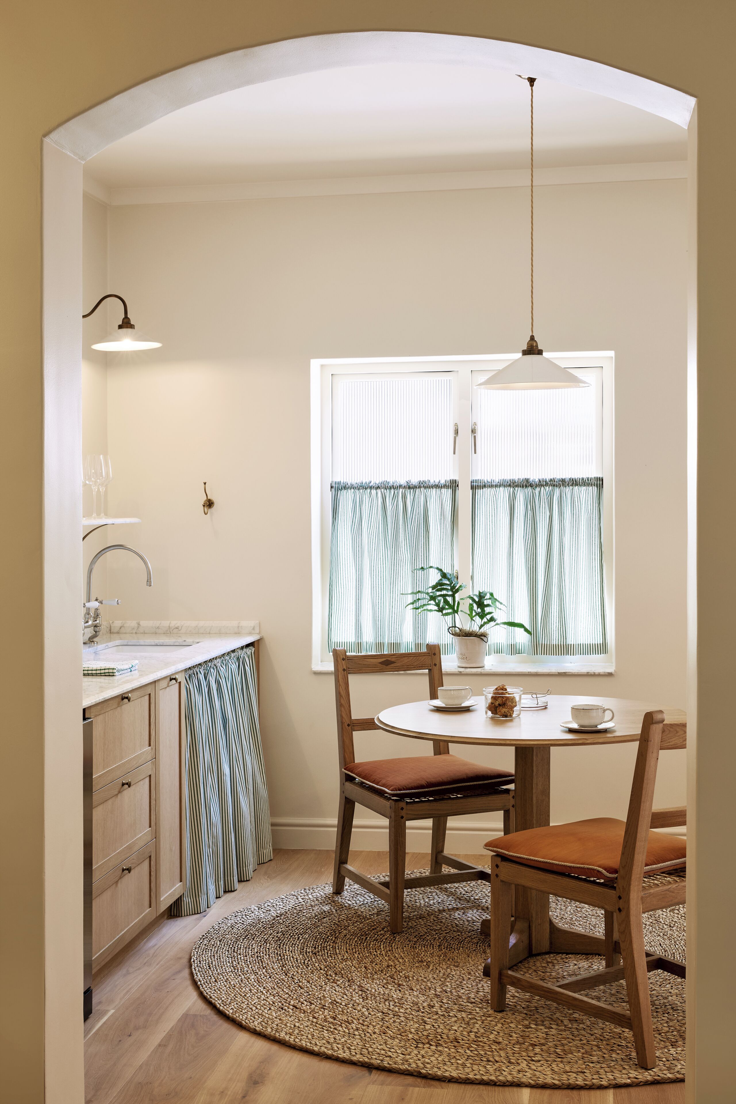 A compact kitchen with a round table, wooden chairs, and a hanging light fixture.