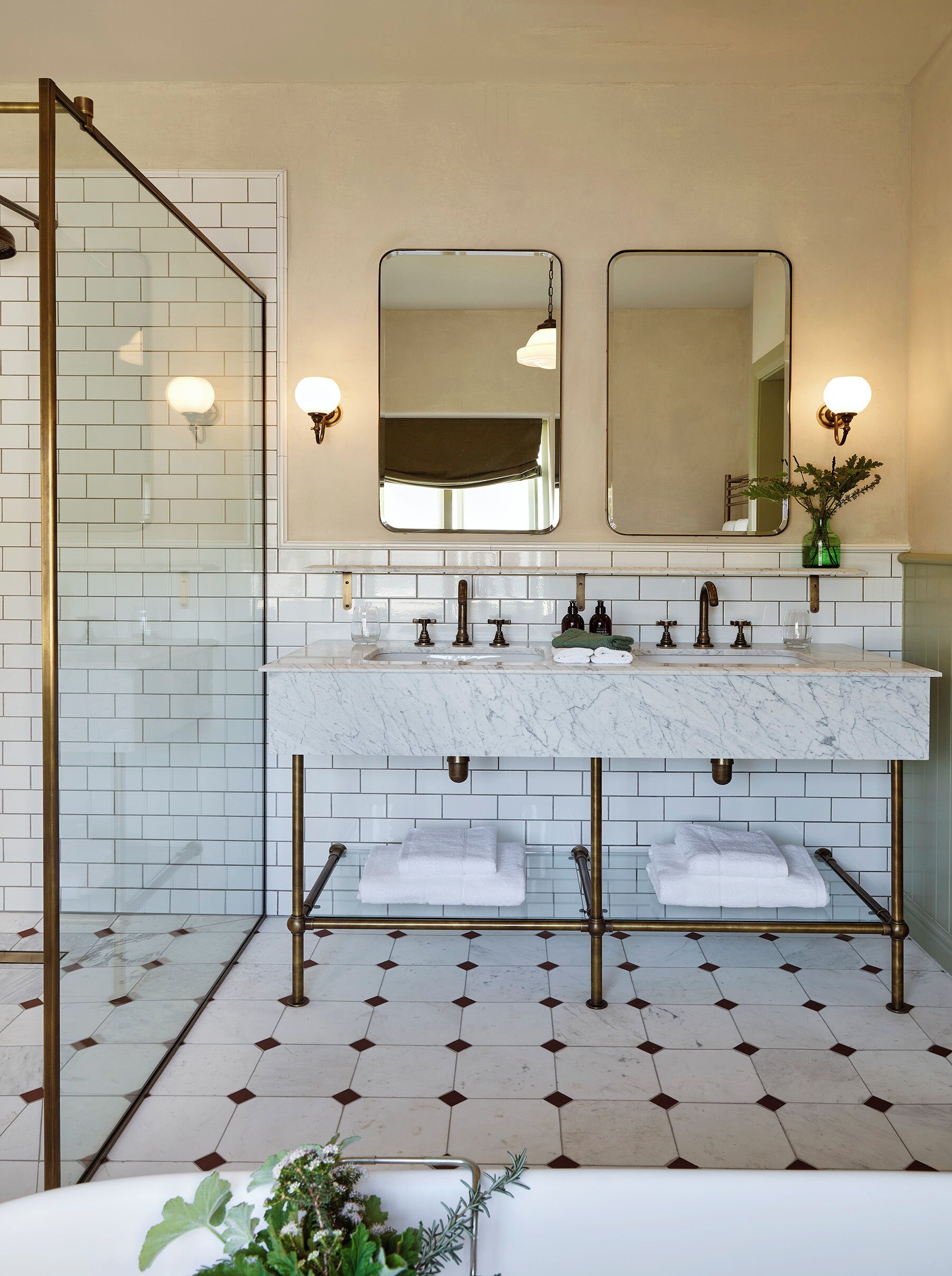 A bathroom with a double sink, two mirrors, a glass shower enclosure, and a tiled floor with a diamond pattern.