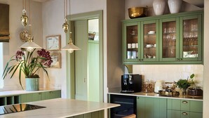 Una cocina moderna con gabinetes verdes, una isla de mármol y lámparas colgantes.