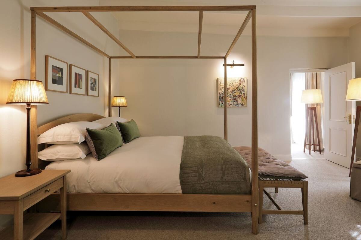 Ein Himmelsbett mit Holzrahmen, zwei Nachttischlampen, ein Nachttisch und eine Bank.