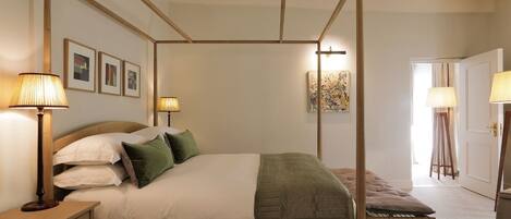 A four-poster bed with a wooden frame, two bedside lamps, a bedside table, and a bench.