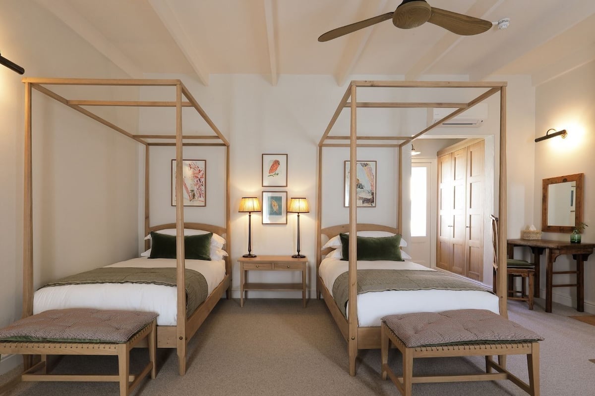 Ein Zimmer mit zwei Himmelbetten, einem Deckenventilator und einem Schreibtisch mit Spiegel.