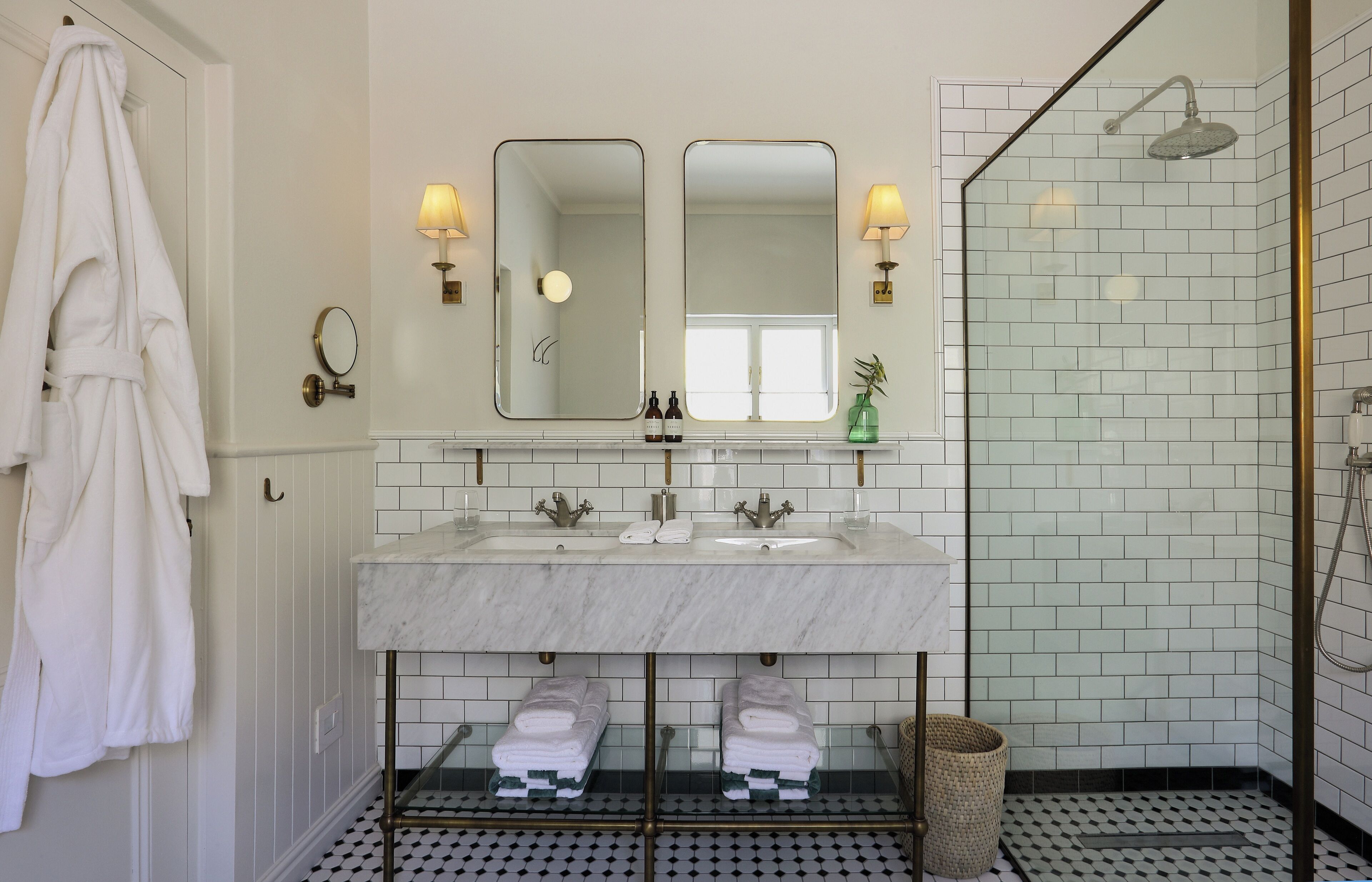 A bathroom with a double sink, two mirrors, and a shower.