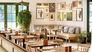 Un restaurante moderno con mesas y bancos de madera, lámparas colgantes y cuadros en las paredes.