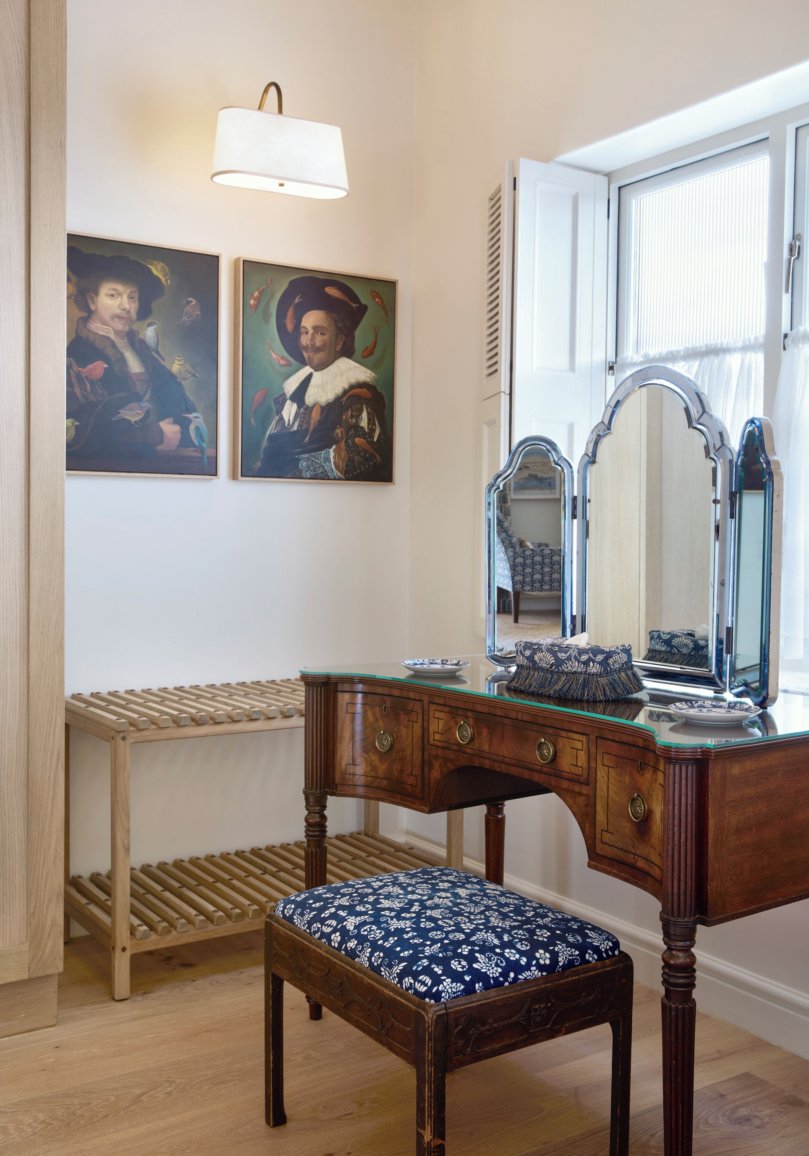 A wooden vanity with a mirror, a bench, and two framed paintings on the wall.