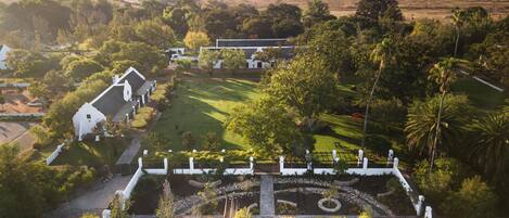 Una extensa propiedad con un jardín formal, edificios blancos y un paisaje montañoso al fondo.