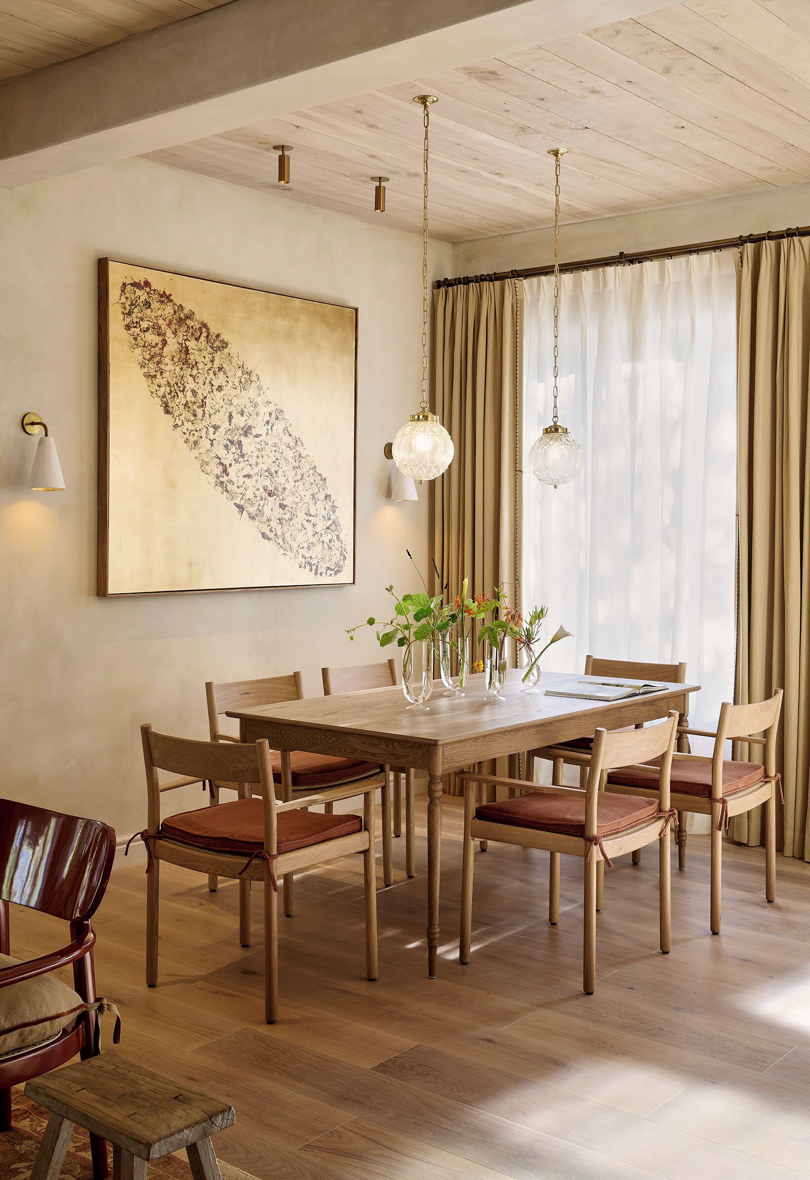 Een eetgedeelte met een houten tafel, stoelen en een groot abstract schilderij aan de muur.