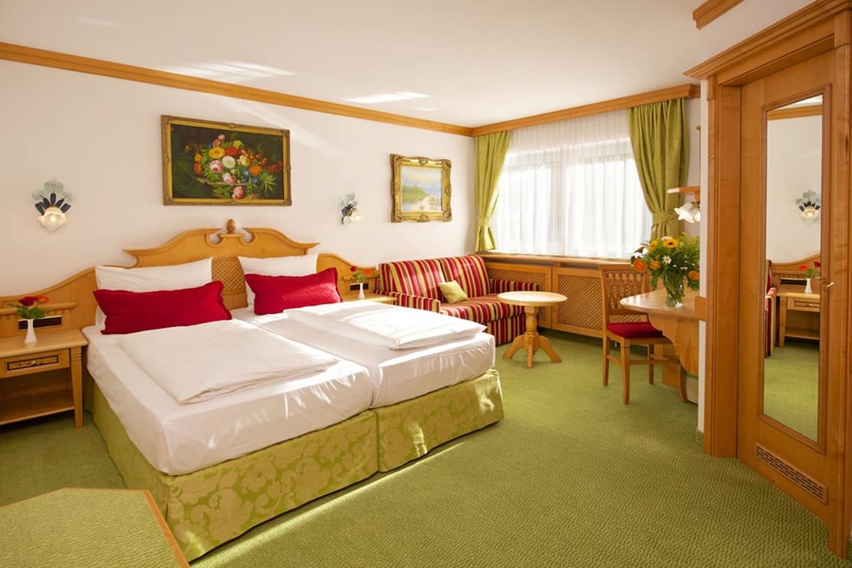 A hotel room with a double bed, a sofa, a small table, and a mirror.