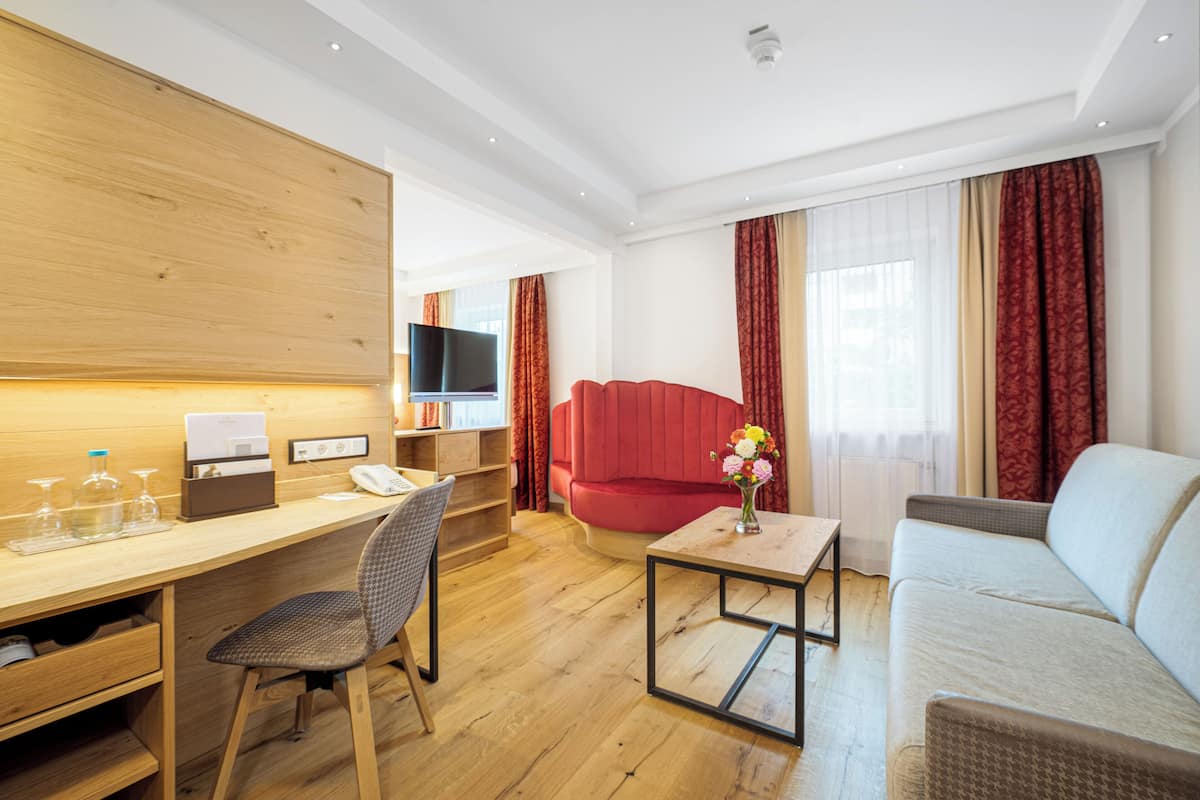 A modern hotel room with a wooden desk, a red sofa, a grey armchair, and a beige sofa.
