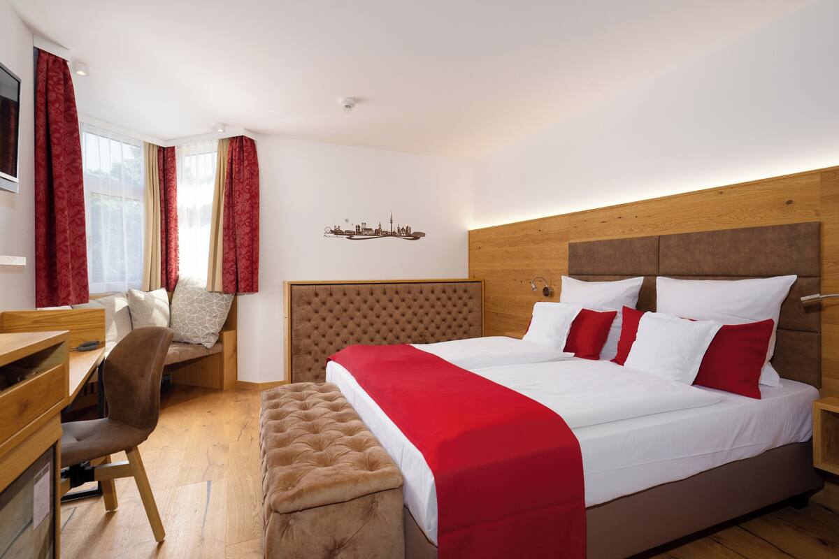 A hotel room with a large bed, a desk, a chair, and a window with curtains.