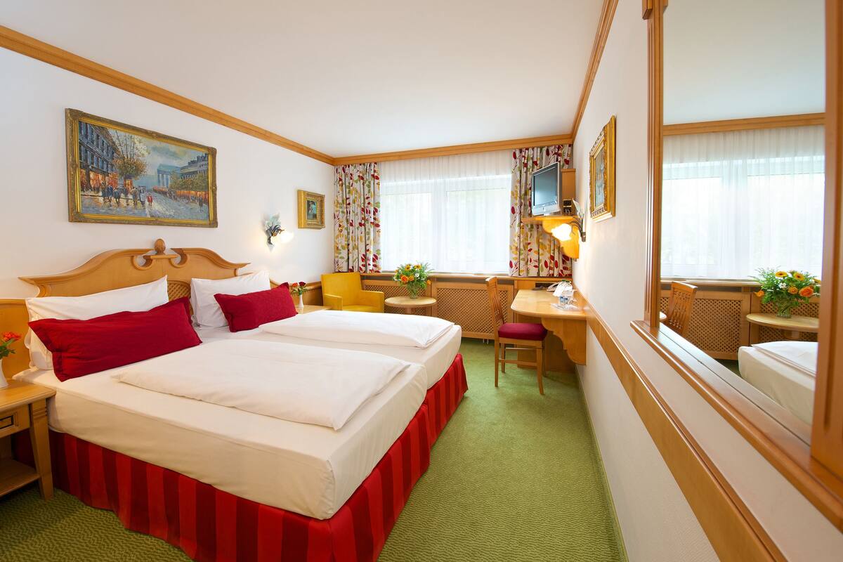 A hotel room with a large bed, a desk, a chair, a television, and a painting on the wall.