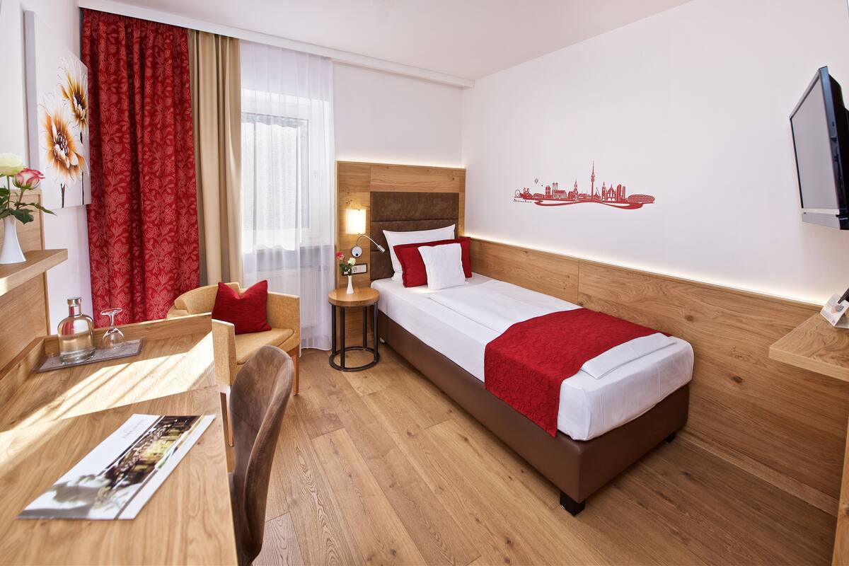 A hotel room with a bed, a desk, a chair, a nightstand, and a TV.