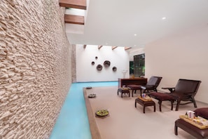 Un interior moderno con una pared de piedra, una piscina y una zona de estar con sillas y una mesa de masaje.