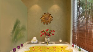 A bathroom with a bathtub filled with yellow flowers, a vase with red flowers, and a decorative wall piece. - Radisson Hotel Khajuraho (Rajnagar)