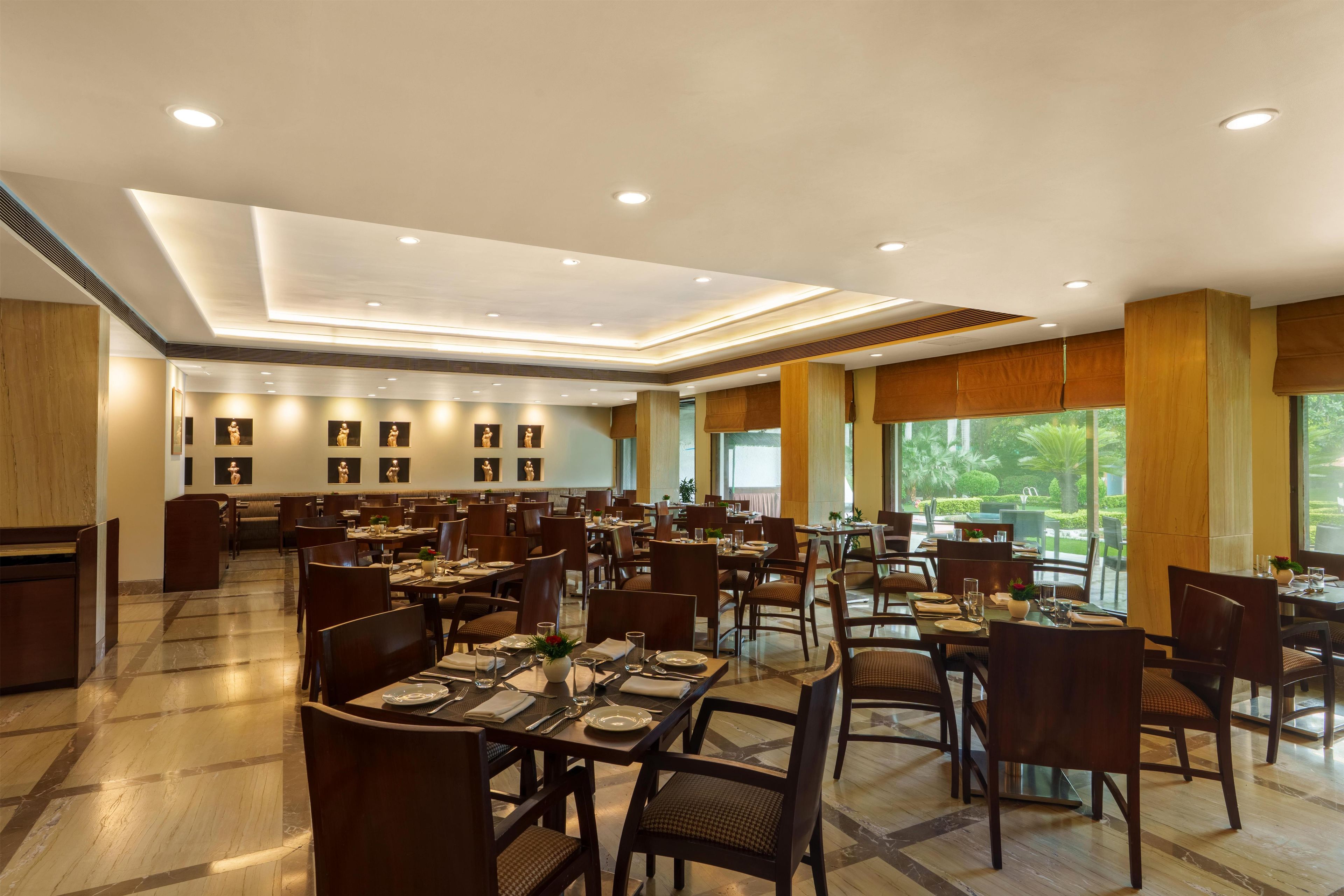 A spacious restaurant with multiple dining tables and chairs, recessed ceiling lighting, and large windows offering a view of the outdoors.