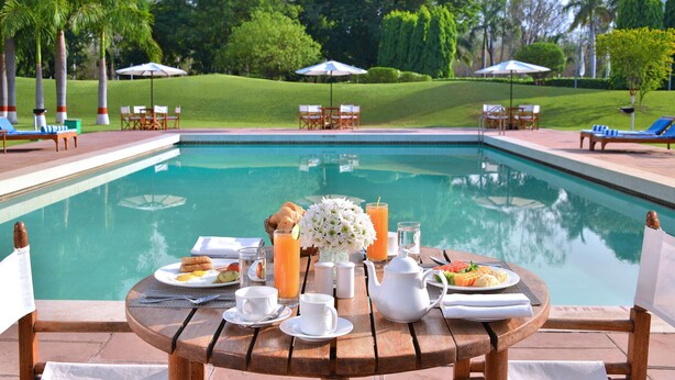 A poolside breakfast setup with a table, chairs, and a view of the pool and surrounding greenery. - Radisson Hotel Khajuraho (Rajnagar)