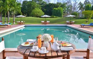 Desayuno junto a la piscina, con una mesa, sillas y vistas a la piscina y la vegetación circundante.