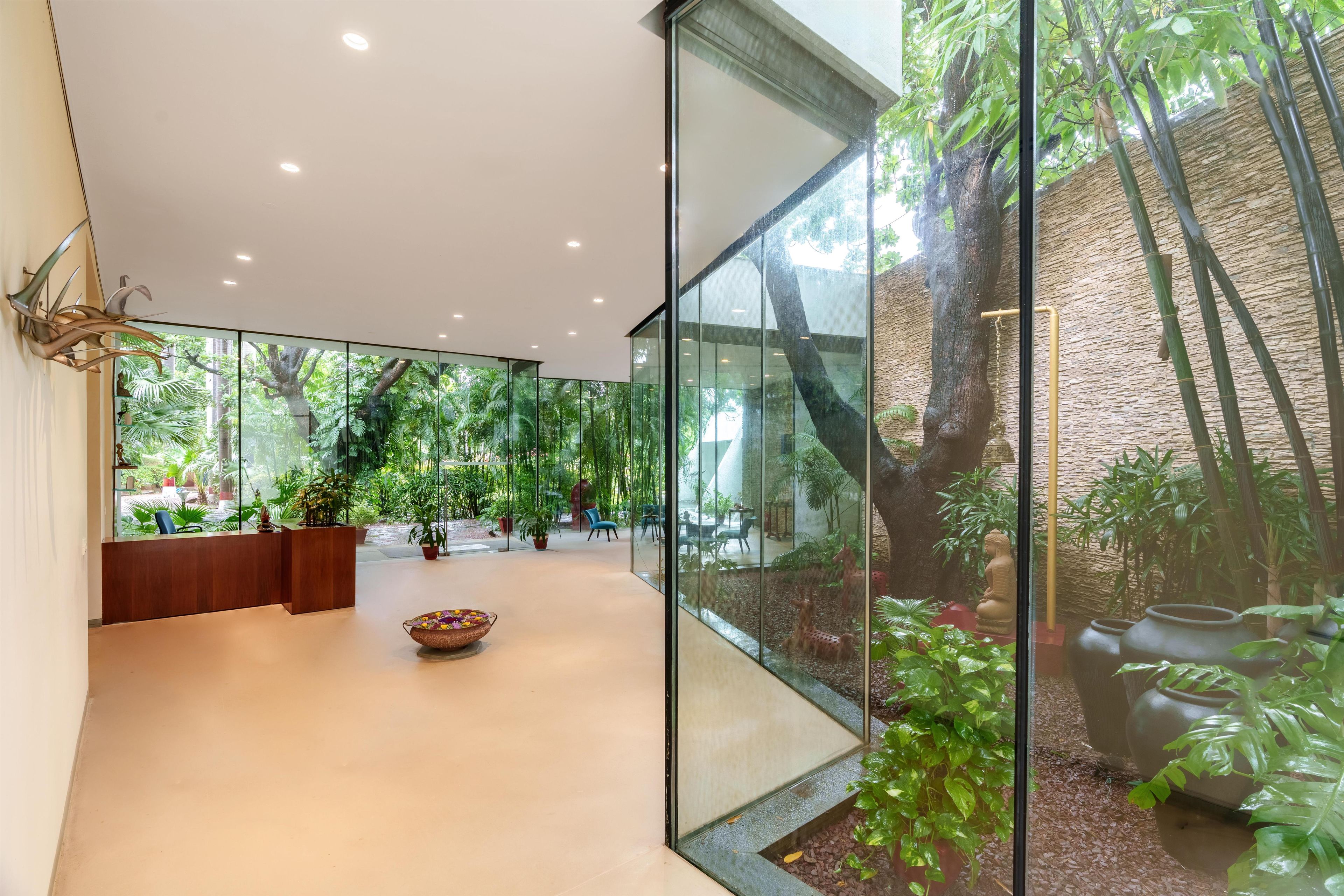 Un interior moderno con paredes de vidrio, una recepción y un área de estar central con un cuenco decorativo.