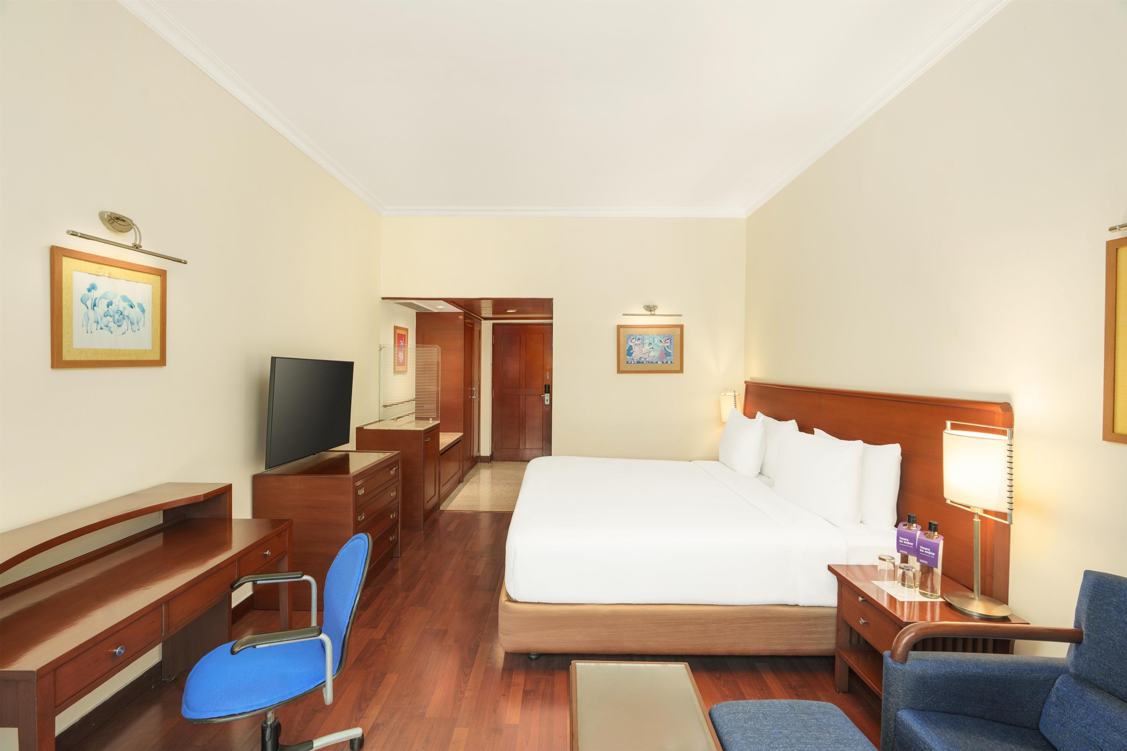 A hotel room with a bed, desk, chair, television, and artwork on the walls.