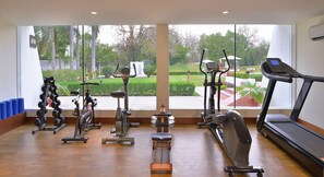 A gym with various exercise equipment, large windows, and a view of a landscaped garden. - Radisson Hotel Khajuraho (Rajnagar)