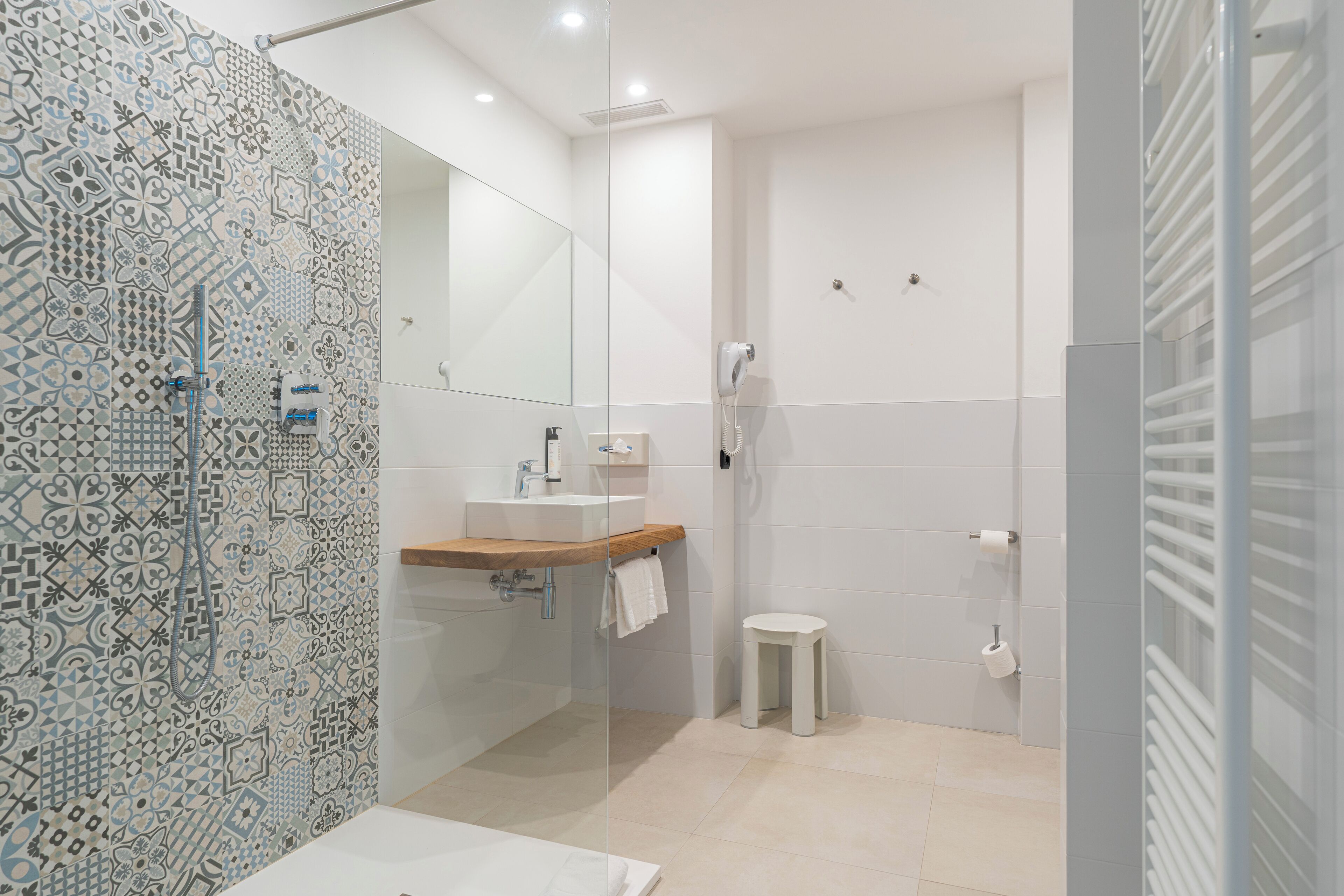 Un baño moderno con baldosas estampadas, cabina de ducha de vidrio, lavabo con encimera de madera y retrete.