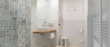 Un baño moderno con baldosas estampadas, cabina de ducha de vidrio, lavabo con encimera de madera y retrete.