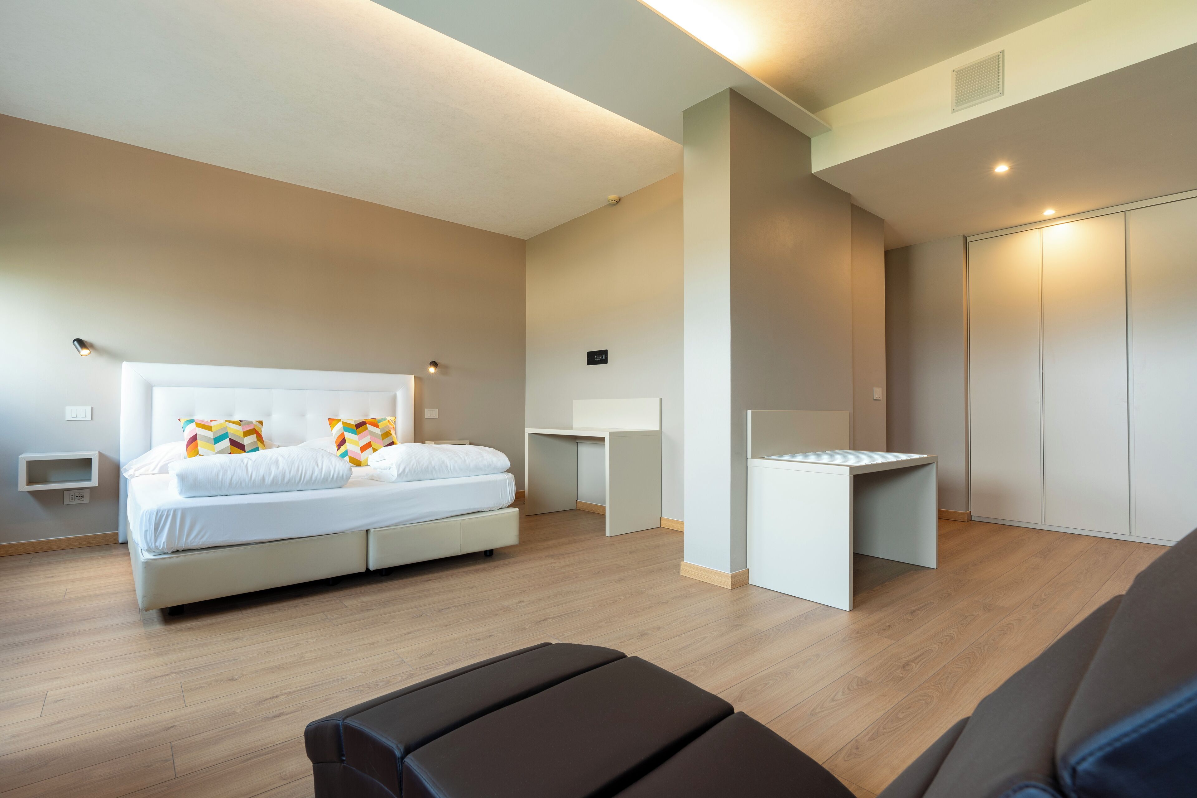 Un dormitorio moderno con cama, mesitas de noche, un escritorio y un armario.