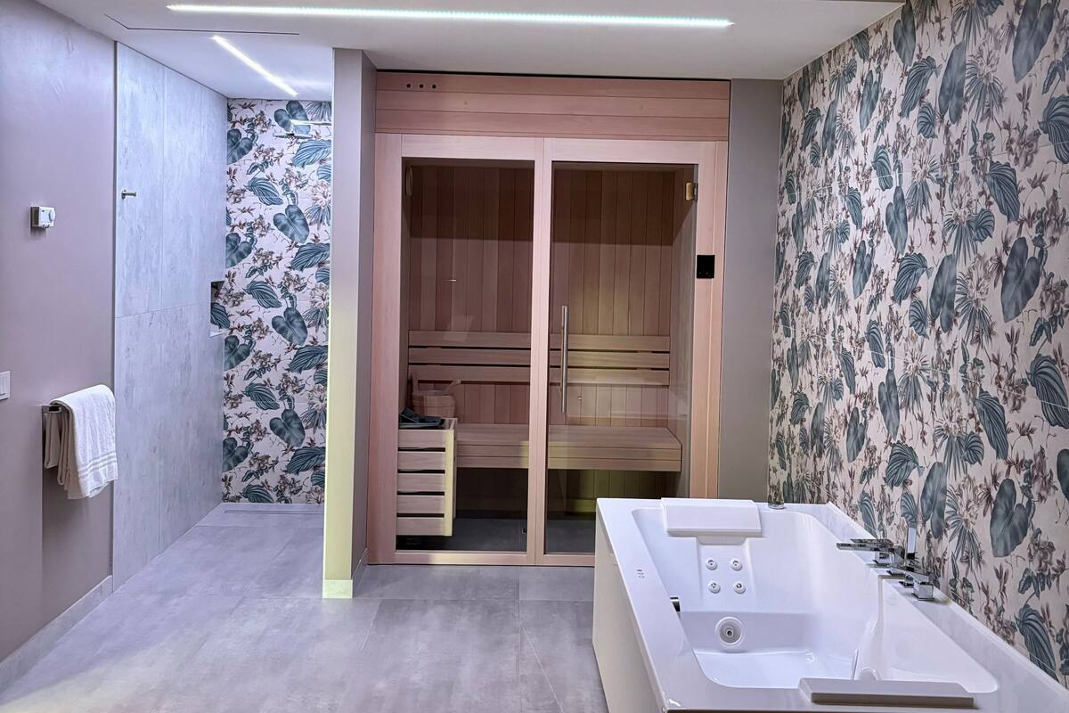 A modern bathroom with a large bathtub, wooden storage closet, and floral wallpaper.